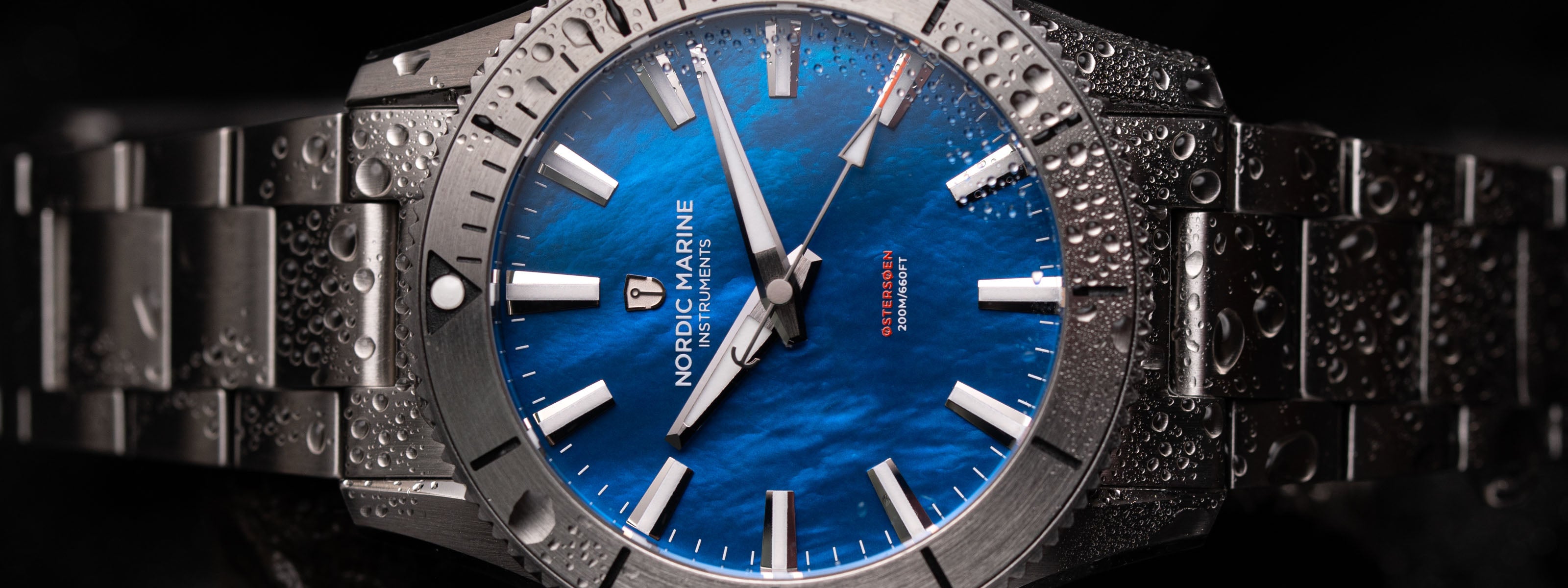 Dive watch with blue mother of pearl dial and metallic band on a dark background