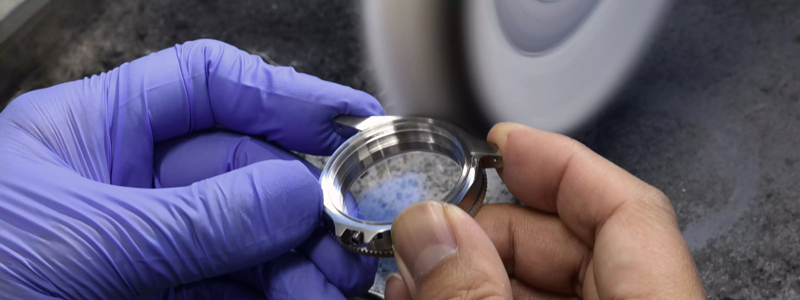 Person wearing purple gloves polishing a steel watch case with a polishing machine